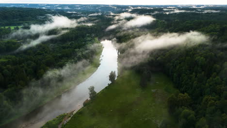 beautiful drone flyover following a magical river surrounded by trees. white mist blanketing the scenic valley of gauja national park in sigulda, latvia.