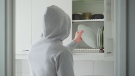 man with a hoodie putting plates into kitchen cabinet