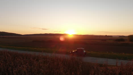 Viaje-Por-Carretera-A-Través-Del-Campo-Al-Atardecer,-Disparo-De-Arco-Aéreo