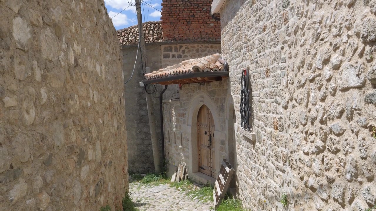 Fortezza di Kruja, Albania, vicolo acciottolato tra mura di pietra che conduce a una porta di legno ad arco