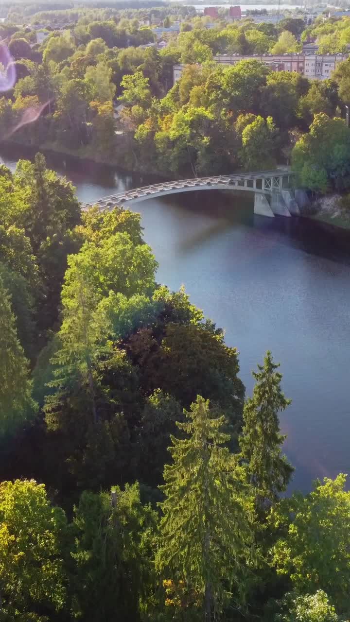 Vertical drone flight over a river and a bridge, surrounded by green trees in September, suburban area, forward dolly shot