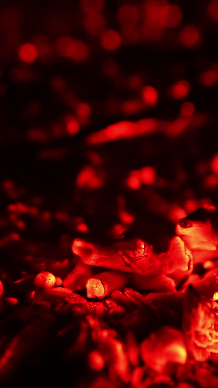 Hot red embers left from the campfire. Light smoke raises up from the charcoal. Close up. Vertical video
