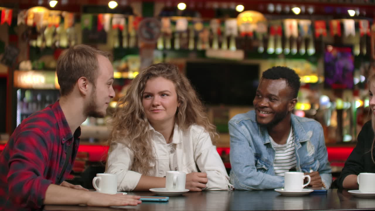 Student meeting in a restaurant and cafe. A man in a shirt tells a story to friends two girls and an African American are listening and laughing. A group of friends spend time together