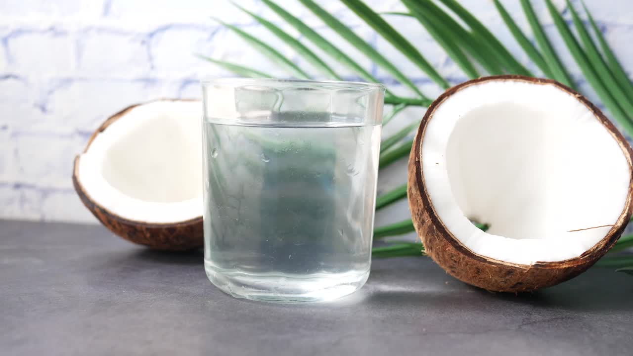agua de coco en un vaso con pedazos de coco y hoja de palma