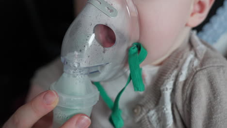 mano de la madre sosteniendo el inhalador en la cara del bebé, niña inhalando del inhalador - primer plano