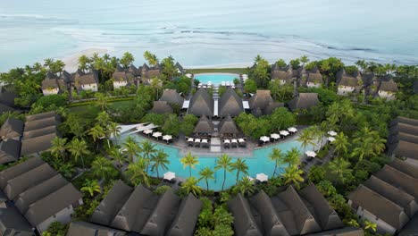luxury oceanside resort with tropical palm tres and pools next to ocean- aerial pull back view