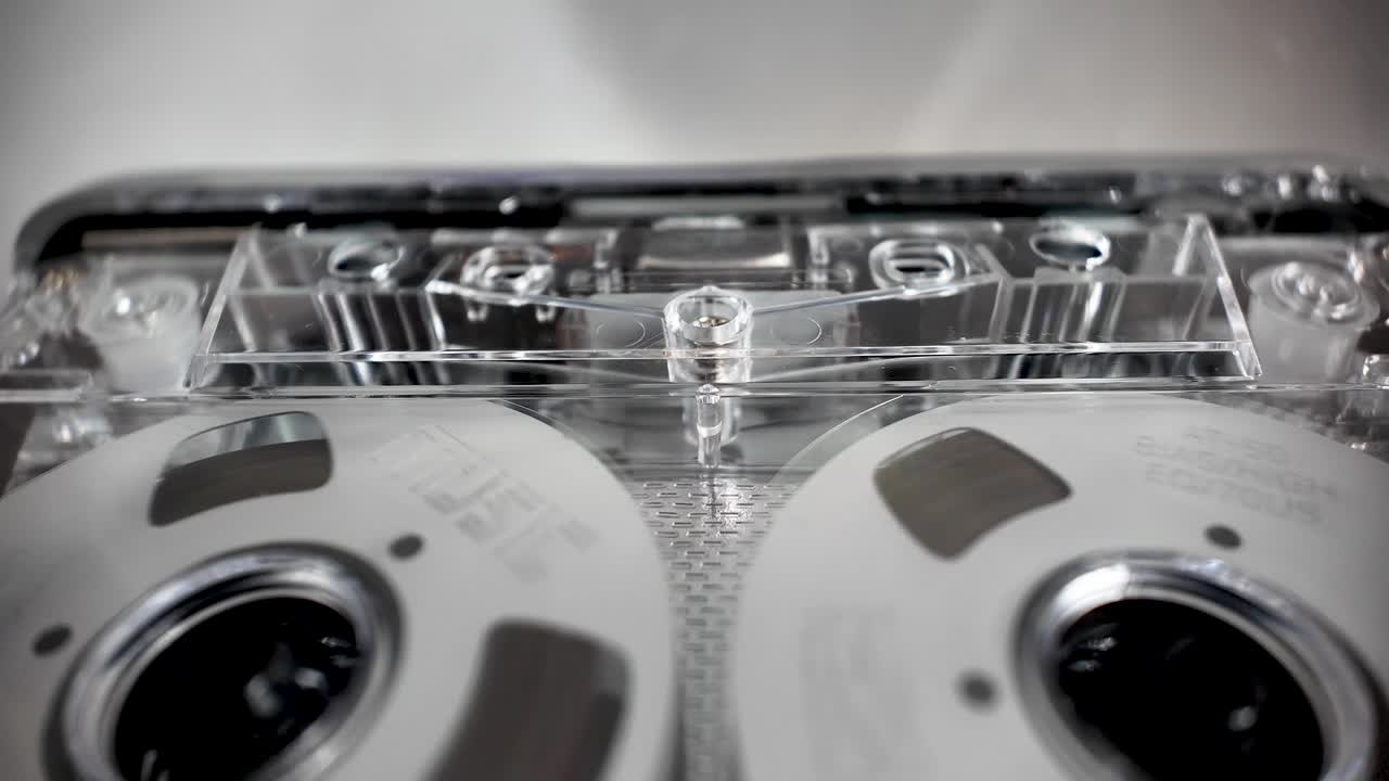 Kassettebåndspoler der snurrer inde i afspilleren, fremviser analog lydteknologi og musik.