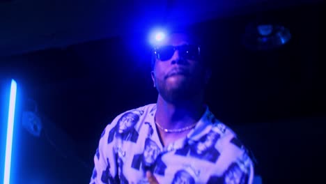 black african male man artist singer rapper showman performs performs concert party on the club stage in dark scenery with neon lights blue theme singing