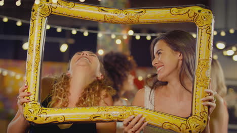 female friends having fun posing with photo booth photo frame at party in bar