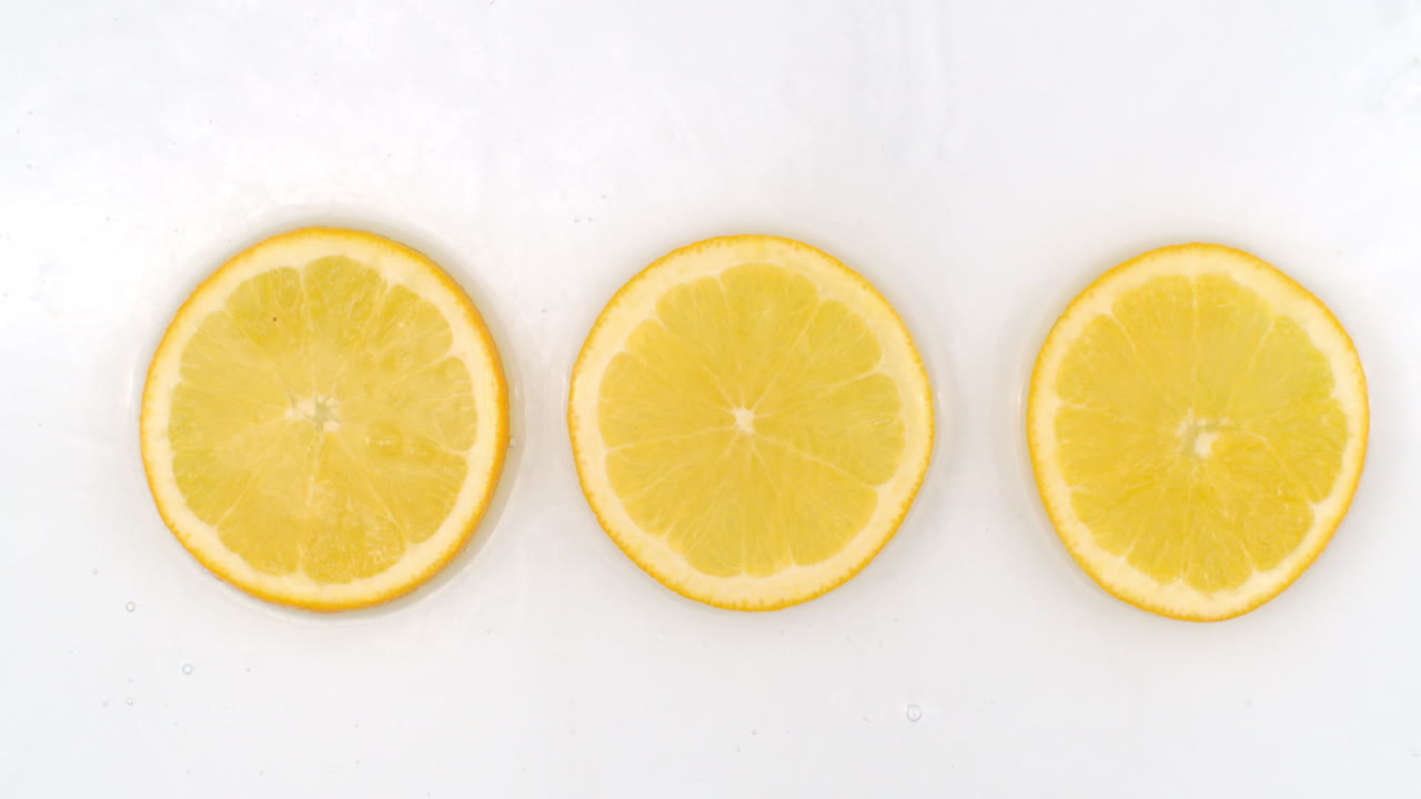 Super Slow Motion Shot of Splashing Water to three orange Slices view from above