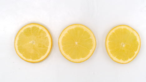 super slow motion shot of splashing water to three orange slices view from above