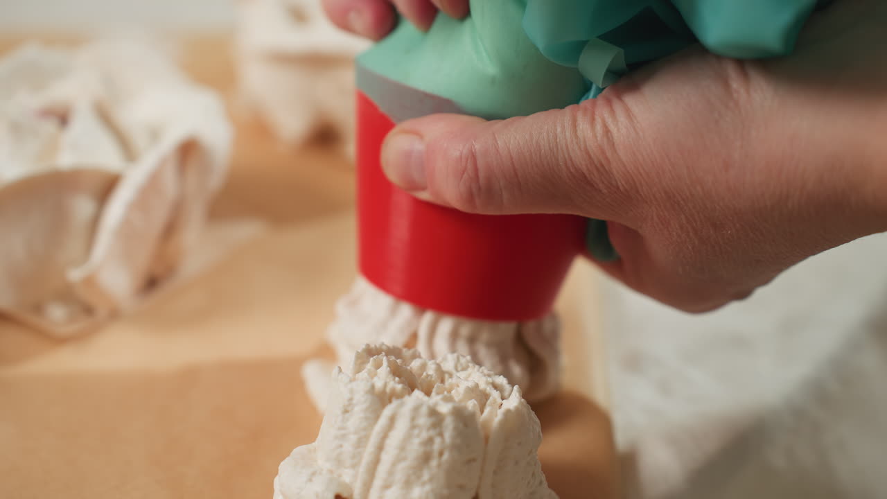 Close up of baker hand pressing piping bag as white dough is released onto parchment paper to form a shaped dessert, showcasing technique and texture during precise baking preparation