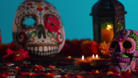 close up of decorated skulls and masks surrounded by candles and flower petals celebrating mexican holiday of dia de muertos or day of the dead against blue background 3