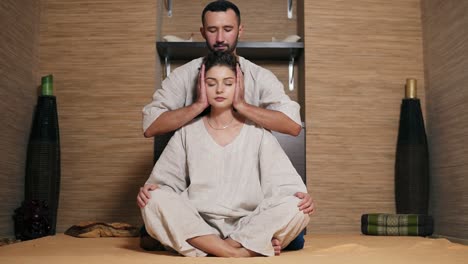 매력적인 태국 마사지사는 그녀의 뒤에 앉아 젊은 여자의 머리를 마사지입니다 2