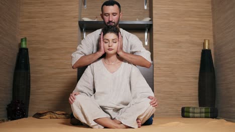 attractive thai massagist is massaging young woman's head sitting behind her 2