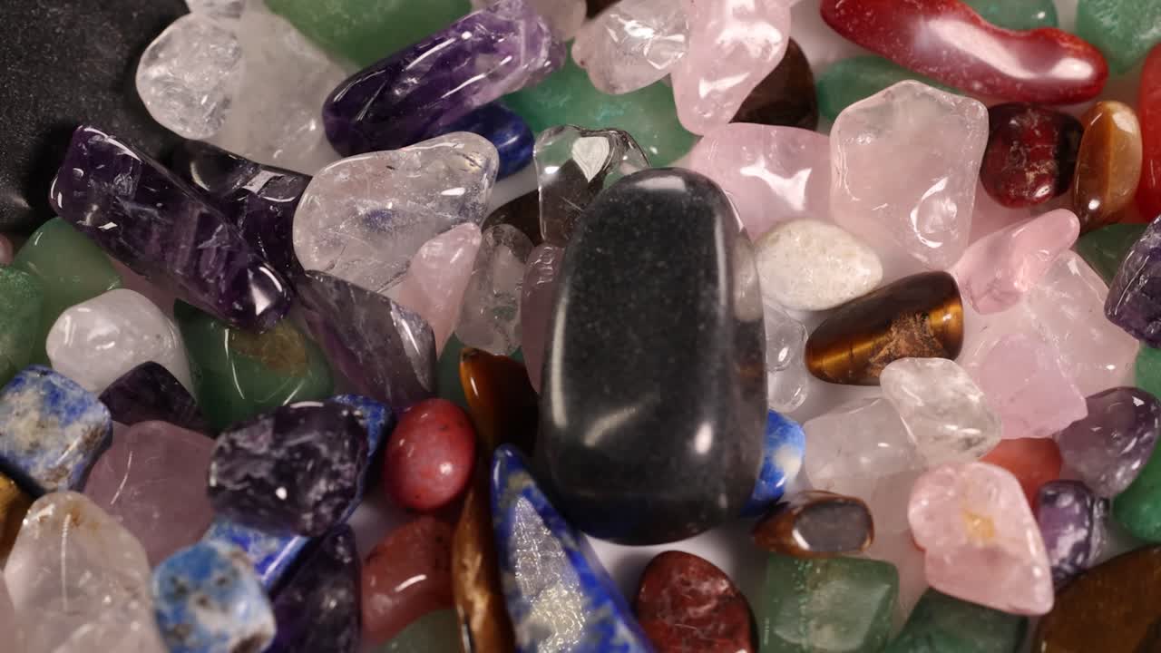 Chakra stones rotate on a vibrant bed of various gemstones, showcasing their colors and textures under soft lighting