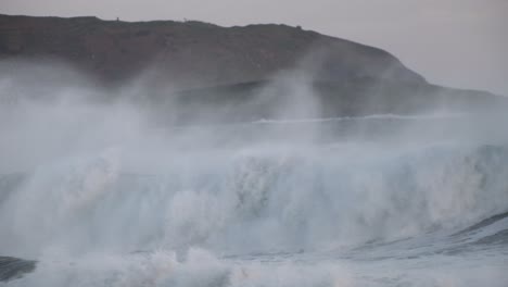 Huge-waves-with-spray-and-foam-rolling-over-coastal-area-at-sunset-blue-hour