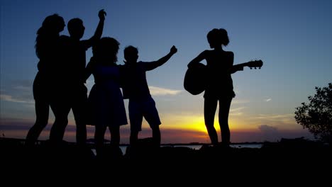 silhouette of friends dancing by ocean at sunset