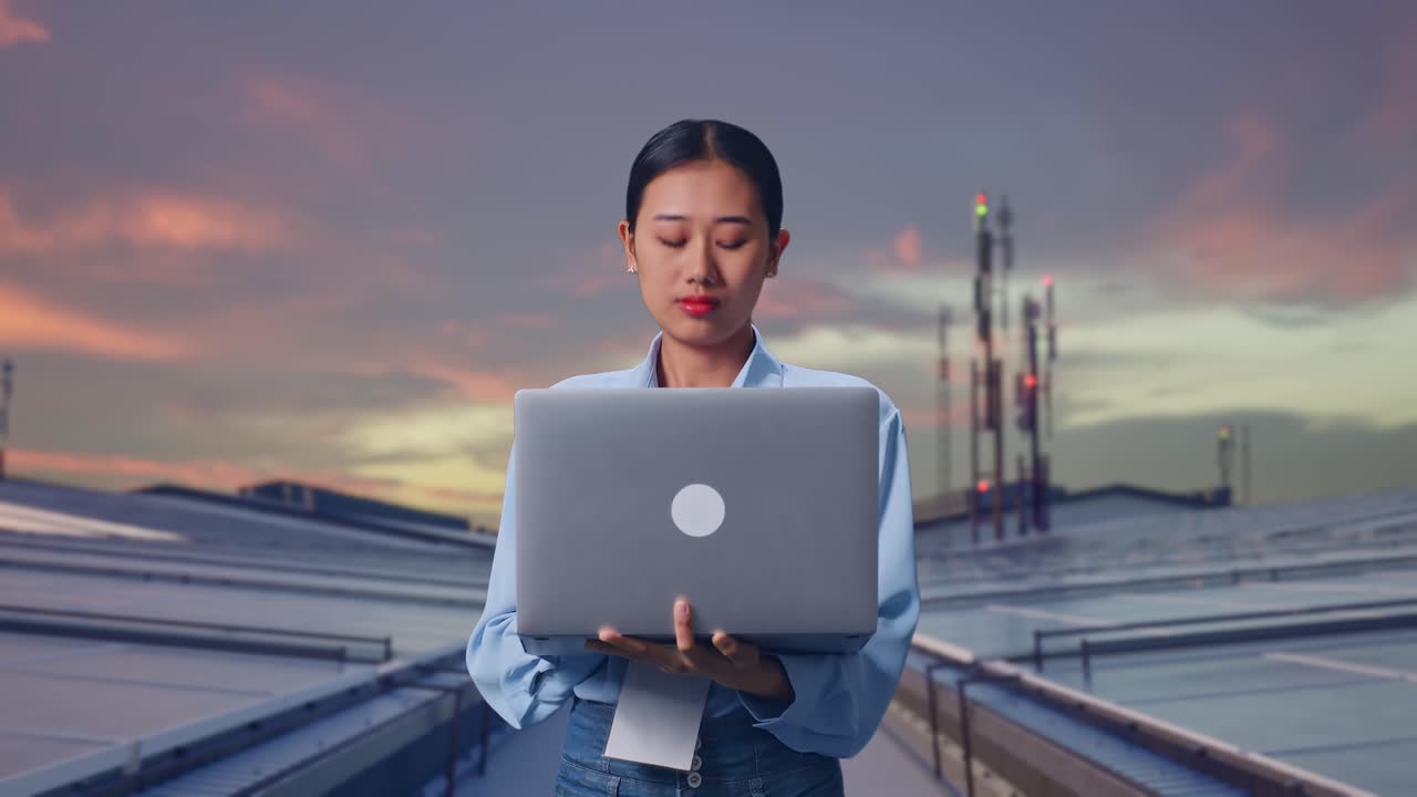 Aziatische vrouw met haar laptop, inspecteert industriële zonnepanelen op het dak, ze observeert door rond te kijken voordat ze zich concentreert op haar laptop