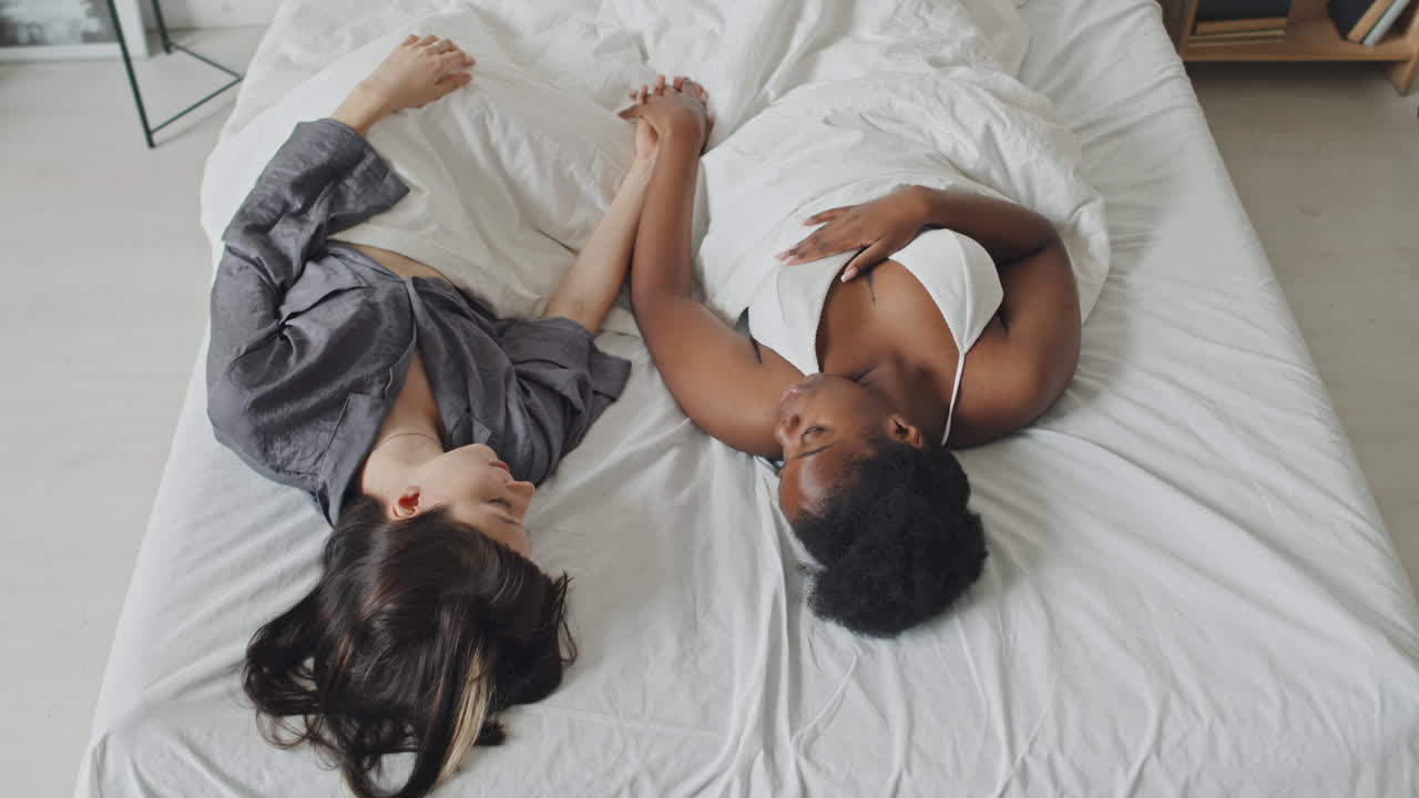 Lesbian Couple Lying on Bed and Holding Hands