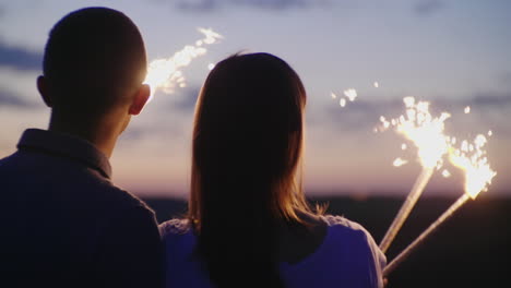 una pareja joven divirtiéndose con fuegos artificiales miran hacia adelante frente a ellos los fuegos artificiales están ardiendo en el