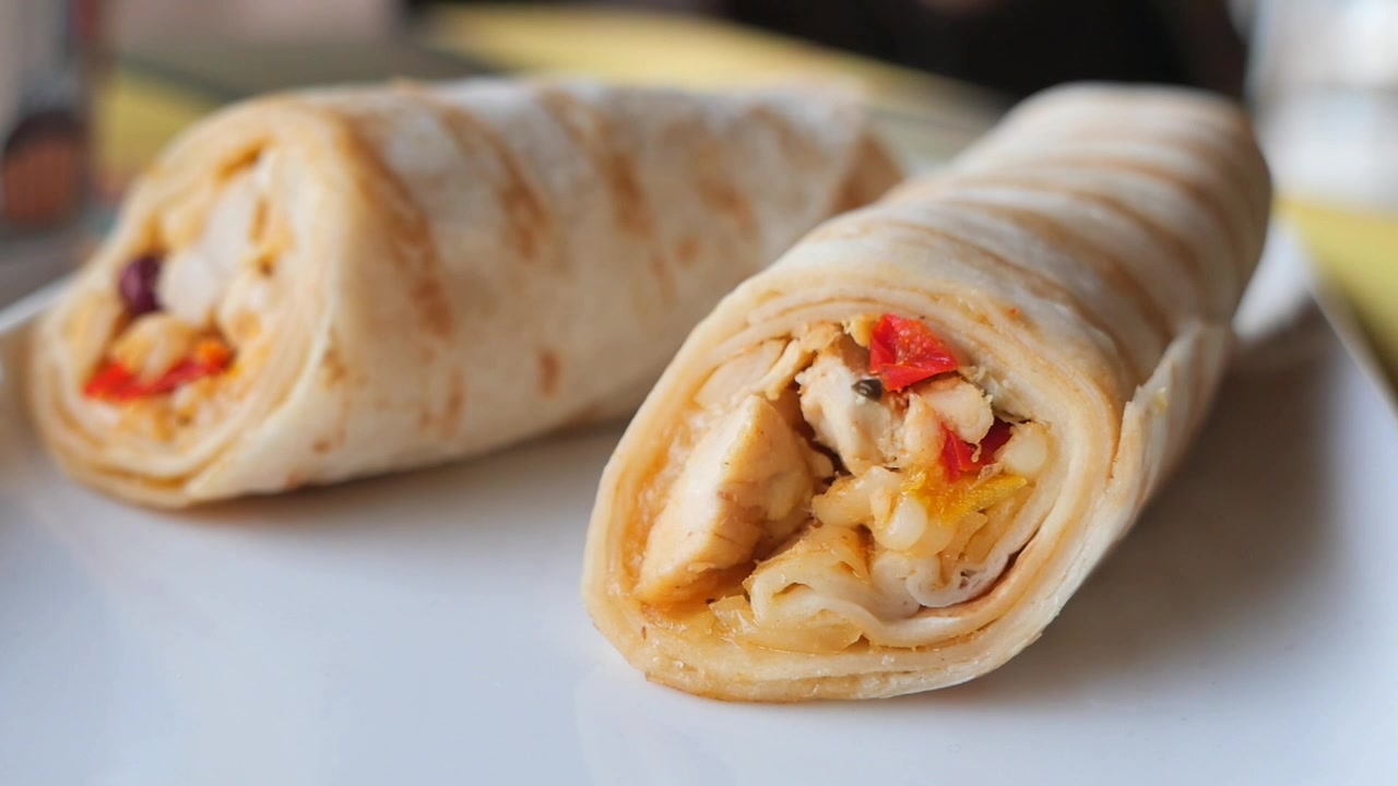 Hand Picking Up a Fresh Chicken Wrap from a Plate