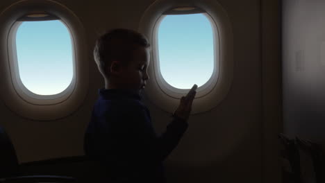 in cabin of plane little boy holding a phone and watching a video