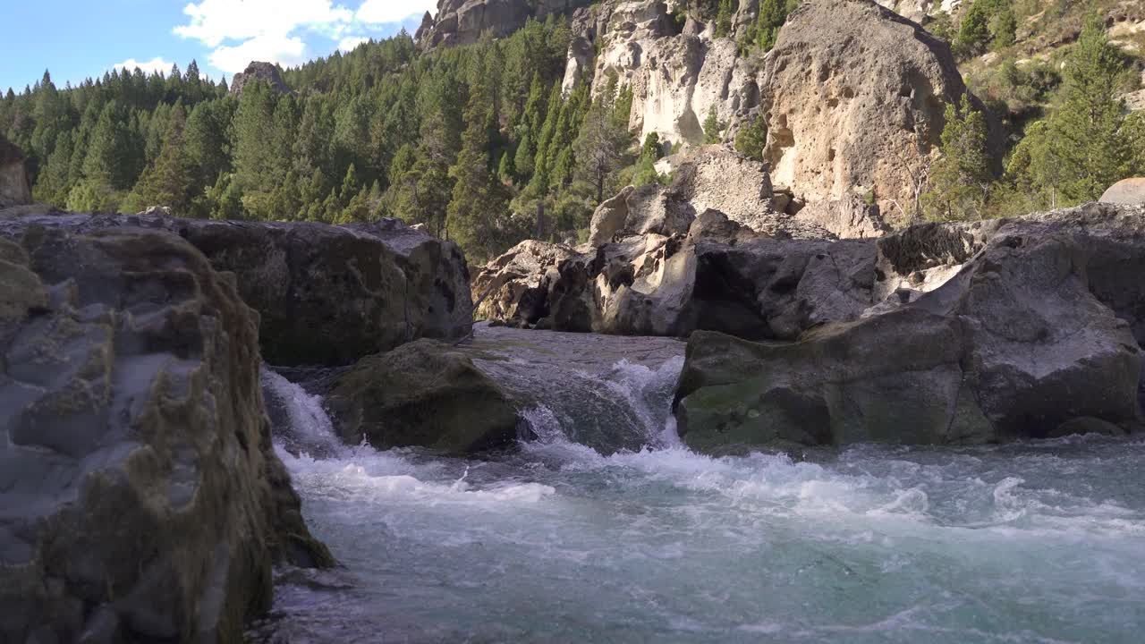 tiro estático de ángulo bajo de un arroyo rocoso que fluye al aire libre durante el día soleado y la cordillera verde en el fondo
