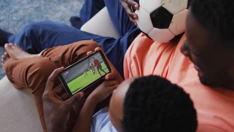 composite of father and son at home watching rugby match on smartphone