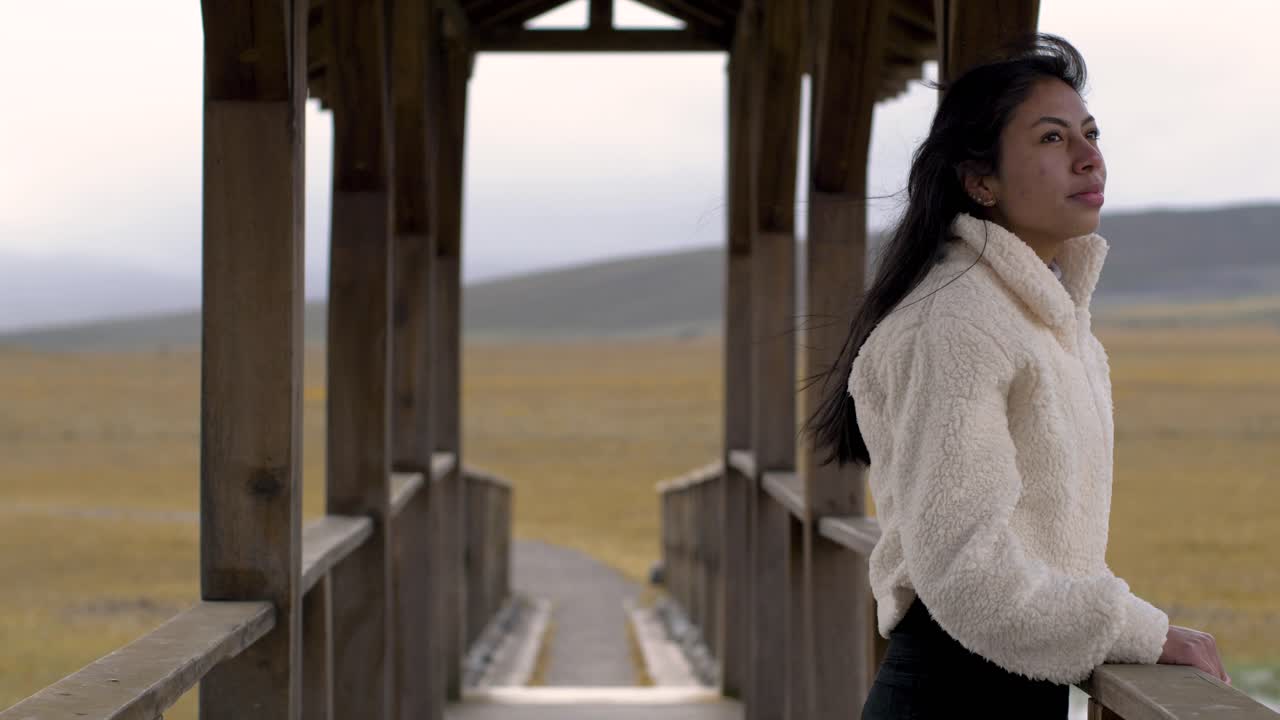 Medium view of woman fixing hair and walking to other side of bridge gazing out