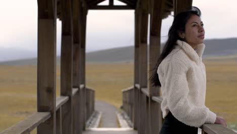 medium view of woman fixing hair and walking to other side of bridge gazing out