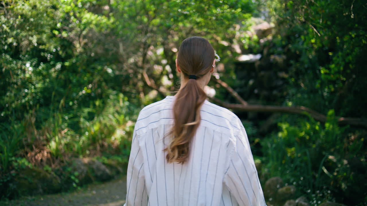 웃으며 카메라를 향해 돌아다니는 빛 정원을 산책하는 유쾌한 여자. 걸어가는 소녀