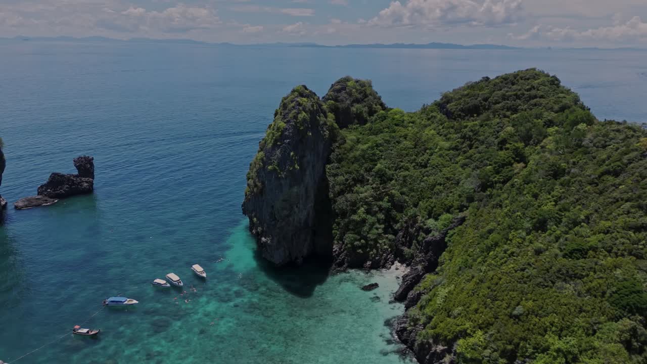 Drone pan-left showing boats and towering rock formations over clear blue sea near Phi Phi Islands, Thailand. Filmed midday with sunny skies.
