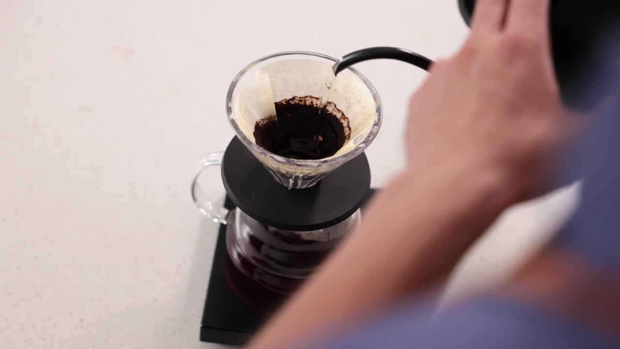 Professioneller Barista bereitet Kaffee im Filterpapier-Stil mit der Pour-over-Methode zu, indem er heißes Wasser gießt, um ein koffeinhaltiges Getränk aus Kaffeebohnen mit einem Schwanenhalskessel in einem Café-Restaurant zu brühen.
