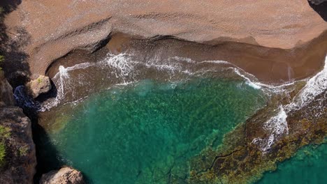 el dron desciende en la playa santu pretu, una bahía de playa de arena negra, mientras las olas chocan contra la orilla.