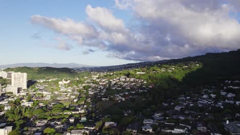 tomada estática de los suburbios fuera de honolulu hawai con residencias construidas a lo largo de la ladera de la montaña tarde en la tarde y las nubes sombrean parte de la ciudad