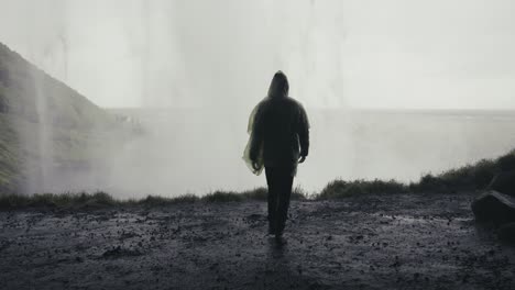 a lone hiker male walks in slow motion towards a waterfall inside a cave