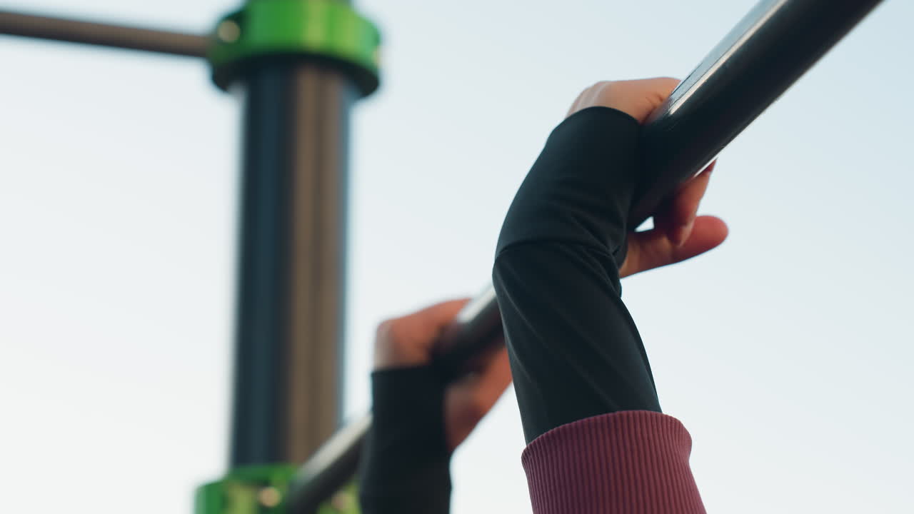 Sky view of athlete hands gripping horizontal bar for balance during urban outdoor workout on rubber floor beneath clear blue sky emphasizing strength focus and stability in fitness routine