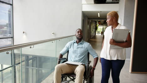 discussing work, diverse colleagues in office hallway, man in wheelchair holding tablet