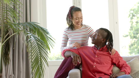 Portrait-of-happy-diverse-couple-embracing-on-couch-in-sunny-room,-copy-space,-slow-motion