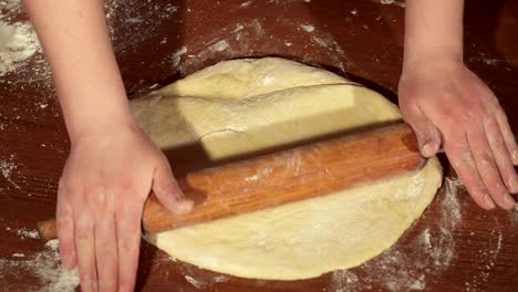 girl rolls out the dough on wooden table.