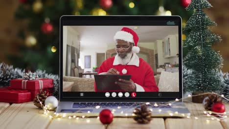 Älterer-Afroamerikanischer-Mann-Im-Weihnachtsmannkostüm-Bei-Videoanruf-Auf-Laptop,-Mit-Weihnachtsbaum