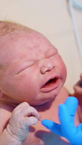 newborn caucasian baby cries bitterly. medic's hand in latex gloves soothes the child touching the chin. close up. vertical video