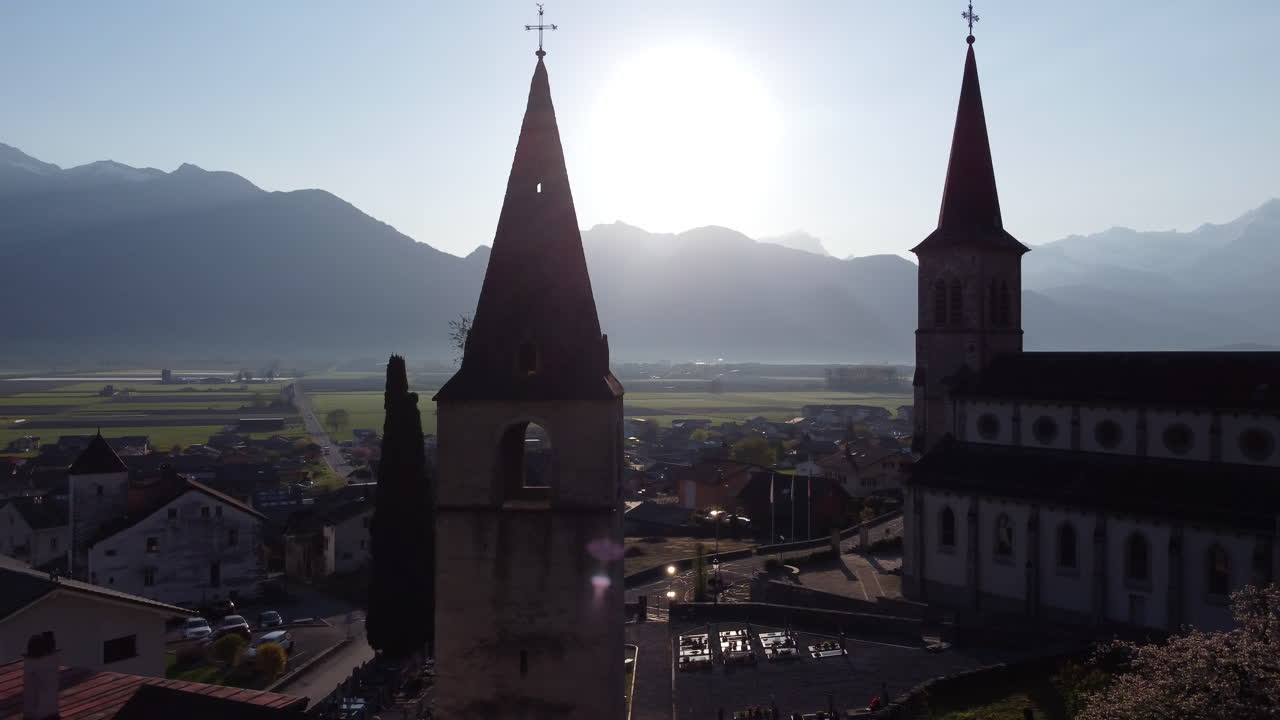 Aerial orbit shot of two churches in Vionnaz, Switzerland silhouetted by the sunlight.