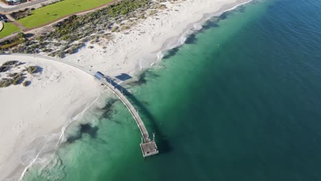 Drone-aerial-pan-up-from-a-pier-to-show-an-expansive-pristine-beach