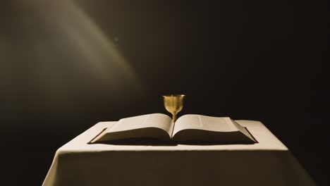 Religious-Concept-Shot-With-Open-Bible-And-Chalice-On-Altar-In-Pool-Of-Light-