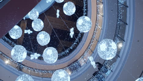 pan shot looking up inside a shopping centre showing large christmas decorations and snow falling