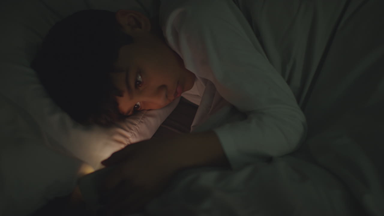 집에서 침실에 누워있는 어린 소년은 밤에 문자 메시지를 보내기 위해 휴대 전화를 사용합니다.