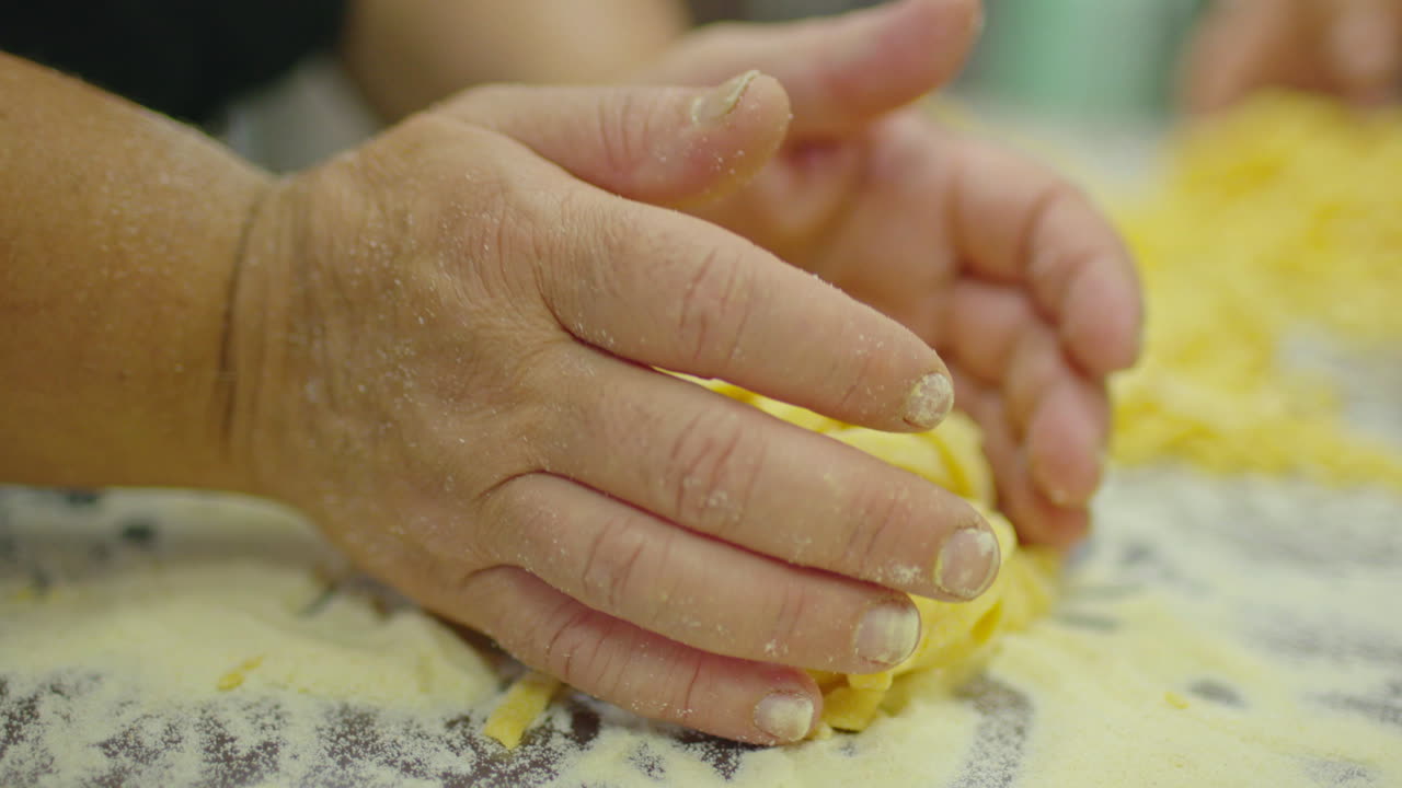 Slow motion close up of woman hands handling a portion of a traditional italian pasta, fettuccine, fettuccini.