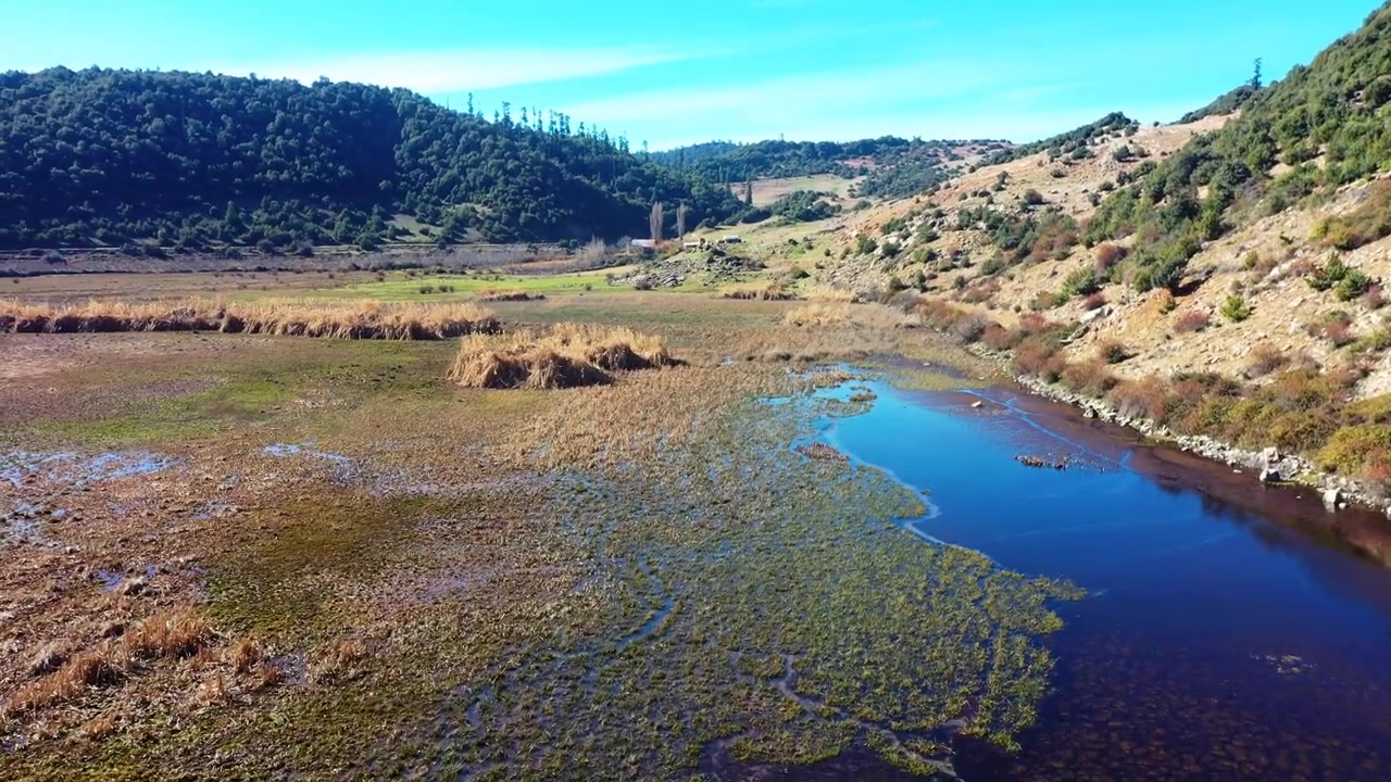 Vista aérea de drone de um rio calmo fluindo por um vale marroquino cênico cercado por colinas e vegetação natural sob um céu azul claro